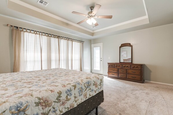 A bedroom with a bed, a dresser, a ceiling fan, and a door.
