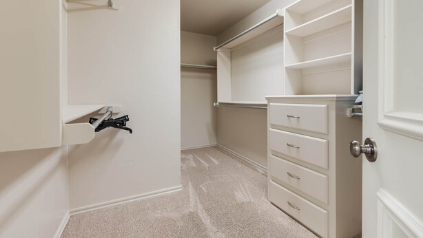 A walk-in closet with open shelving, a hanging rod, and a set of drawers.