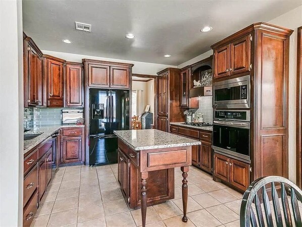 A kitchen with wooden cabinets, a granite countertop, stainless steel appliances, and a tiled floor.