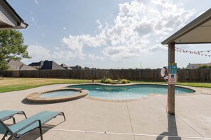 A backyard with a swimming pool, a covered patio, and a wooden fence.