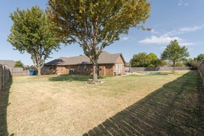 A residential backyard with a brick house, a tree, a swimming pool, and a wooden fence.