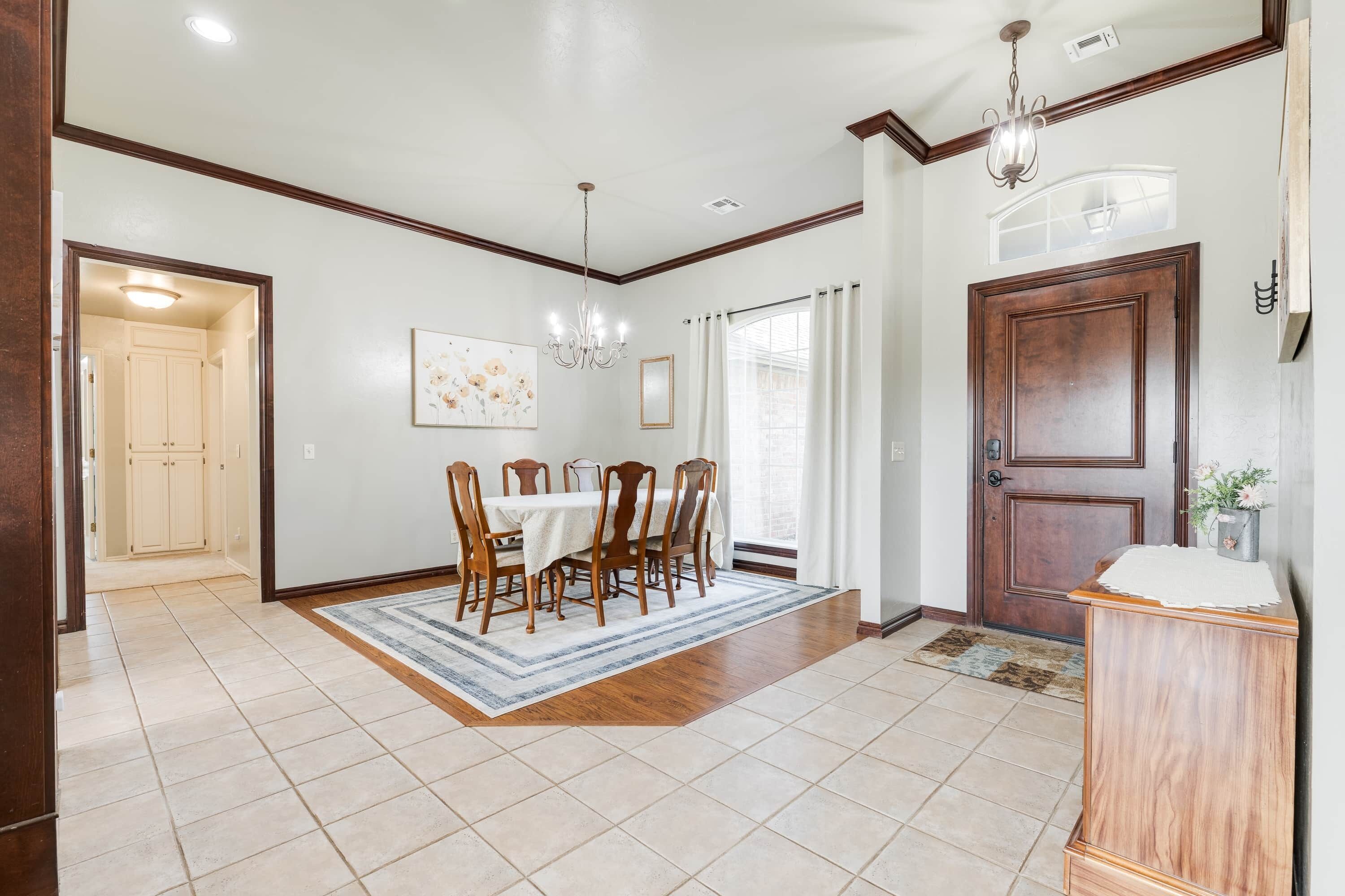 A dining area with a table set for four, a chandelier, and a wooden door with a small plant on the side.