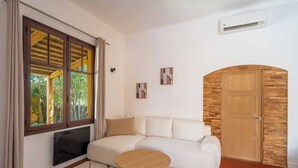Un soggiorno con un divano bianco, un tavolino rotondo in legno, un'ampia finestra con tende e una porta in legno.