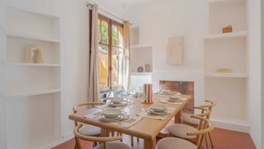 Zona pranzo con tavolo in legno apparecchiata per quattro persone, circondata da sedie, con mensole e camino sullo sfondo.
