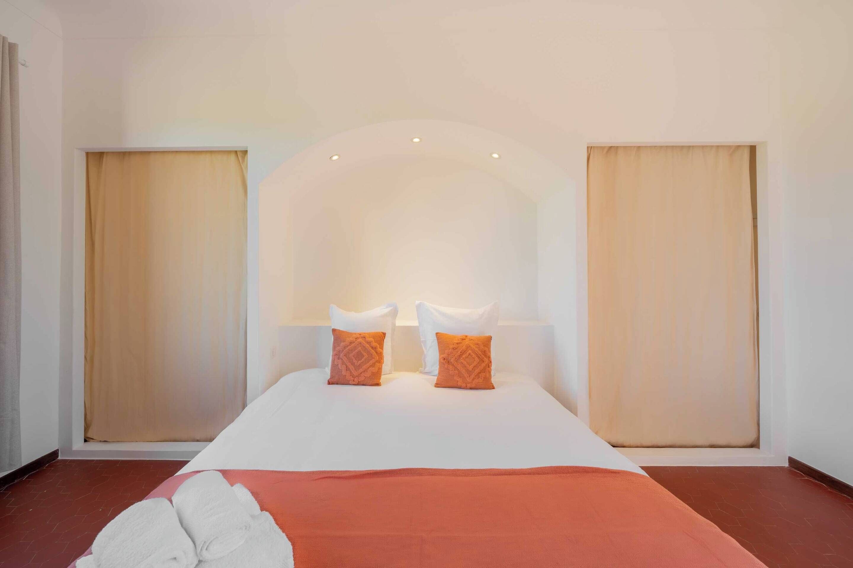 Una habitación de hotel con una cama grande, dos almohadas, un edredón rojo y un cabecero blanco.