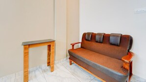 A room with a wooden table, a brown sofa, and a white wall. - Deluxe Tapas (Kozhikode)