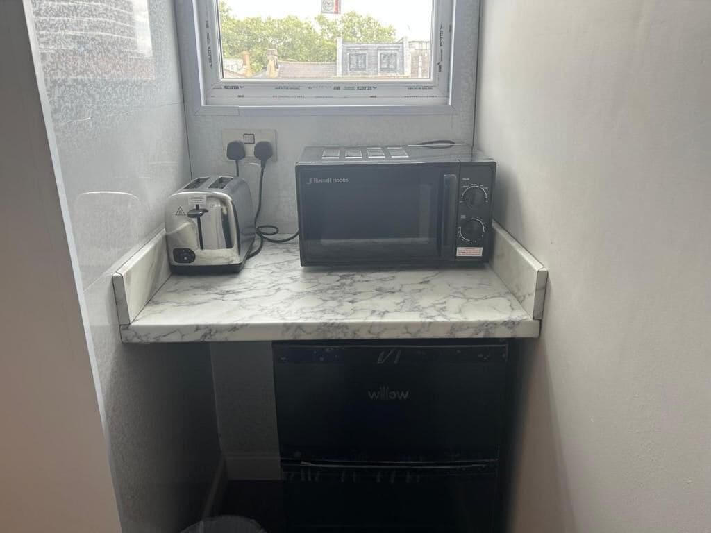 A kitchen with a microwave, toaster, and dishwasher on a marble countertop.