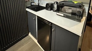 Una cocina compacta con armarios oscuros, una encimera blanca y una cafetera.