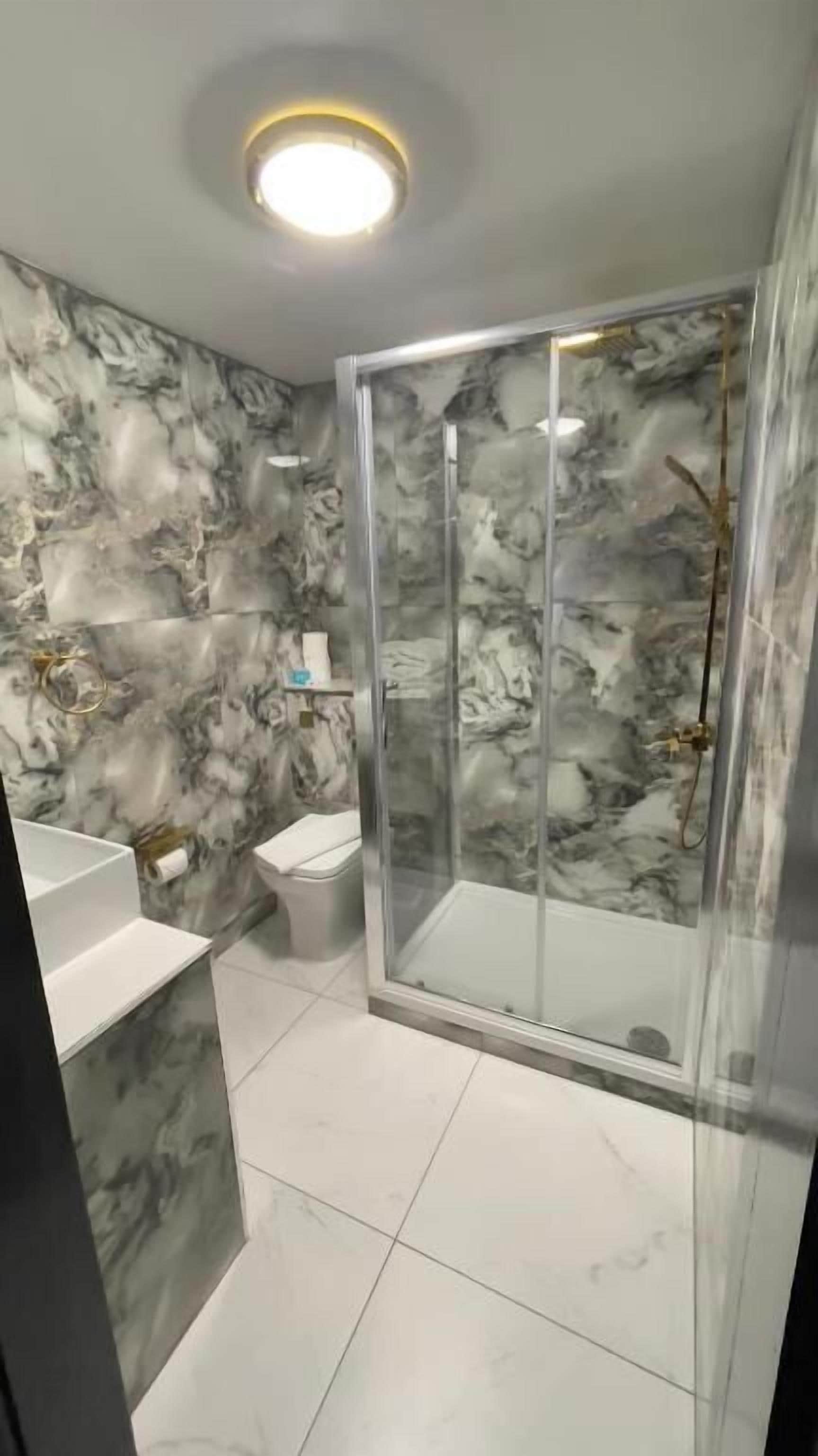 A bathroom with marble walls, a glass shower enclosure, and a white sink.