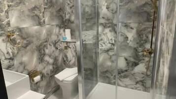 A bathroom with marble walls, a glass shower enclosure, and a white sink.