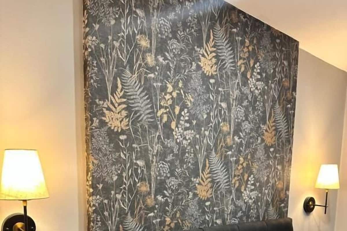 A hotel room with a large bed, two bedside lamps, a remote control on a nightstand, and a floral-patterned headboard.
