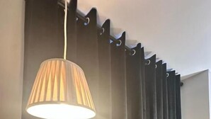 Habitación con cortina negra, lámpara colgante y un interruptor de luz a la vista.