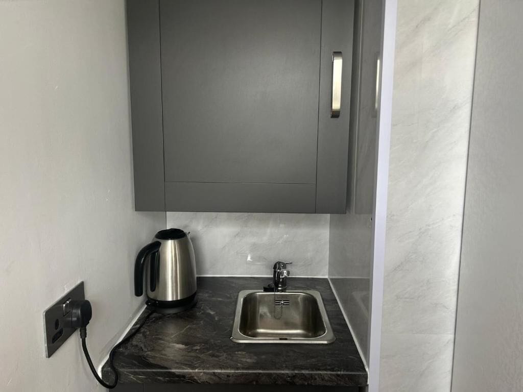 A modern kitchen with a stainless steel sink, a kettle, and a cabinet above the counter.
