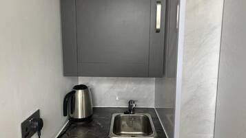 A modern kitchen with a stainless steel sink, a kettle, and a cabinet above the counter.