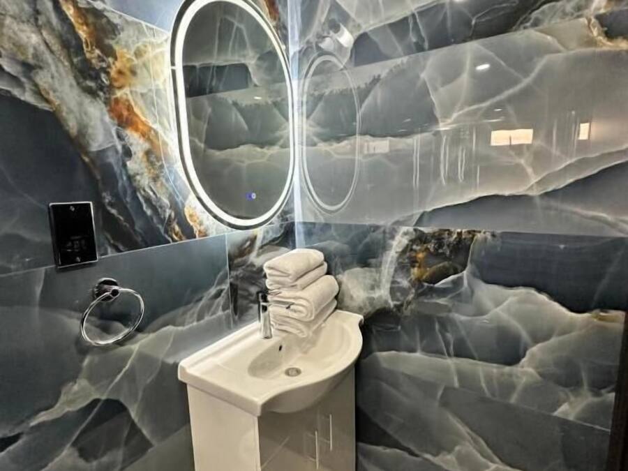 Un baño con pared de mármol, un lavabo, un espejo y un perchero para toallas.
