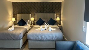 A hotel room with two beds, a headboard with a geometric pattern, bedside lamps, and towels arranged on the beds. - Pasha Hotel London (London)