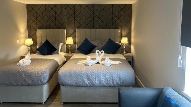 Habitación de hotel con dos camas, cabecero con estampado geométrico, lámparas de noche y toallas dispuestas sobre las camas.