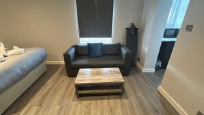 Una sala de estar con sofá, una mesa de centro, una ventana con persianas y una zona de kitchenette.