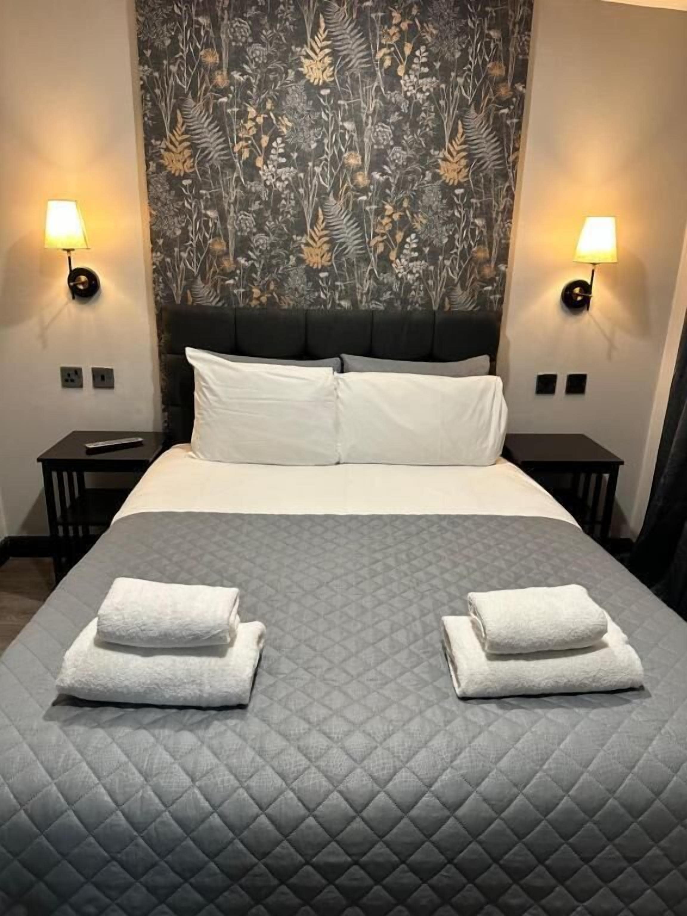 Een hotelkamer met een groot bed, twee bedlampen, een bloemen behang hoofdbord en twee opgevouwen handdoeken op het bed.