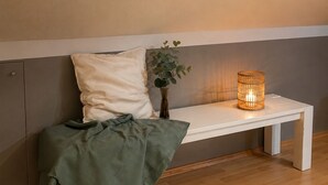 Een bank met kussen, een vaas met plant en een kaars op een tafel.