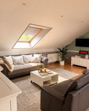 Ein modernes Wohnzimmer mit schrägen Wänden, einem Ecksofa, einem Couchtisch und einem Fernseher.