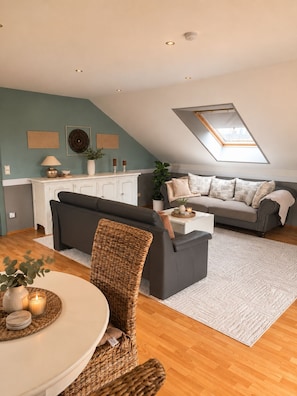 A modern loft apartment with a dining area, a living room with a sofa and a coffee table, a kitchen with a white cabinet, and a skylight. - Green Door Loft: Stylish 160 m² Apartment with Balcony, Garden View, and Dog-Friendly (Ibbenbüren)