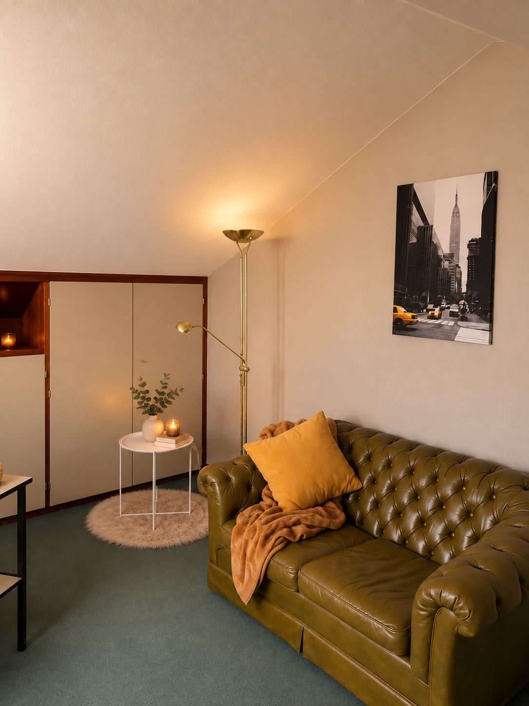 A room with a green leather sofa, a floor lamp, a small table with a plant, and a framed picture on the wall.