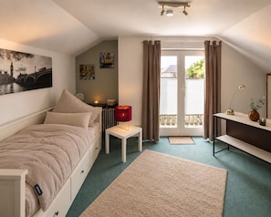 Ein gemütliches Schlafzimmer mit Bett, Nachttisch mit Lampe, Heizkörper und einem Fenster mit Vorhängen.