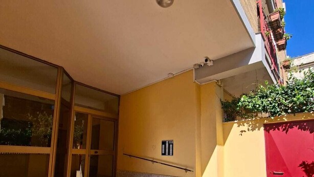 Entrada de un edificio con puerta de vidrio, unos pocos escalones y una puerta roja.