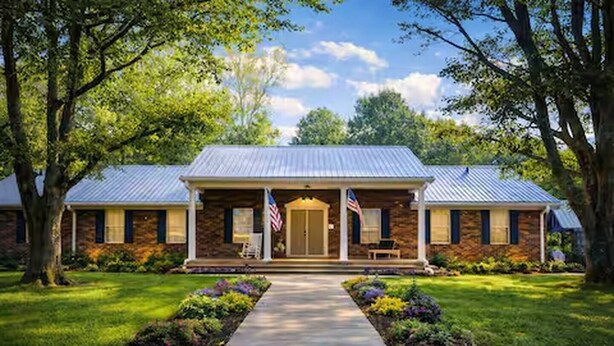 A two-story house with a front porch, a flag, and a well-maintained lawn.