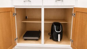 Un gabinete blanco con dos compartimentos abiertos, cada uno con una maleta negra y una mochila negra.