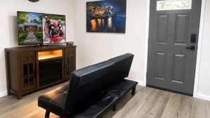 A living room with a black leather sofa, a wooden cabinet, a framed picture, and a gray door.