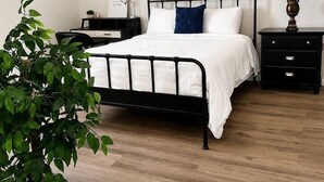 A bedroom with a bed, bedside tables, a ceiling fan, a wall-mounted artwork, and a potted plant.