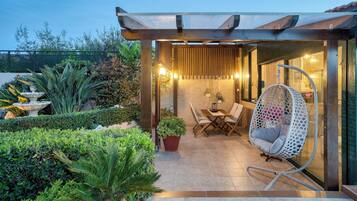 A covered patio area with a hanging chair, a table with chairs, and a variety of potted plants.