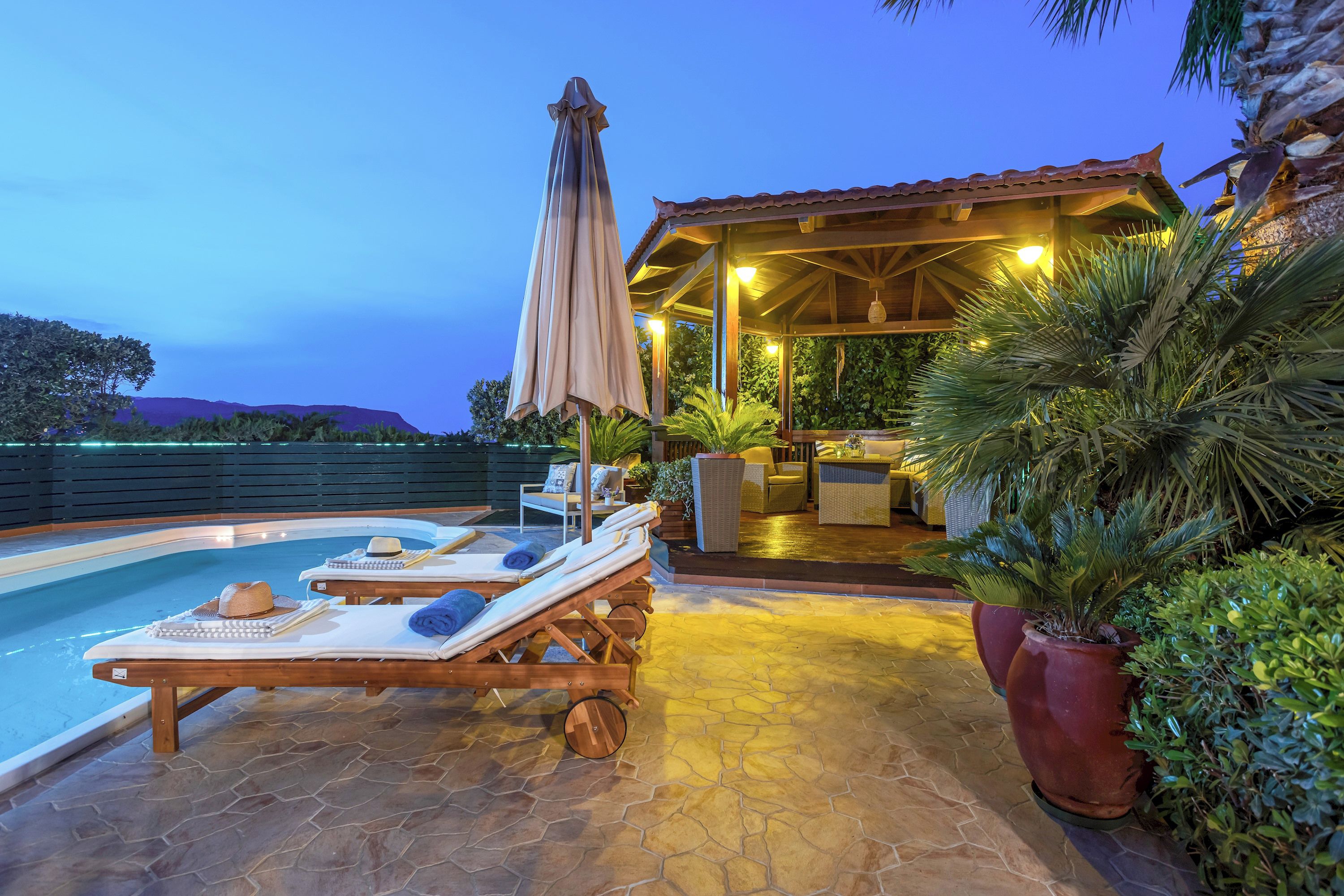 A poolside area with lounge chairs, a covered seating area, and potted plants.