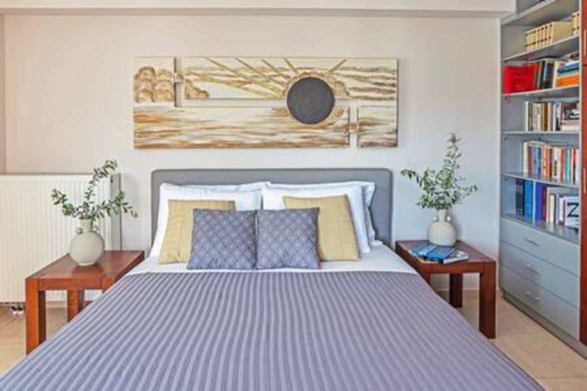 Um quarto bem arrumado com uma cama grande, uma estante de livros e uma obra de arte na parede.