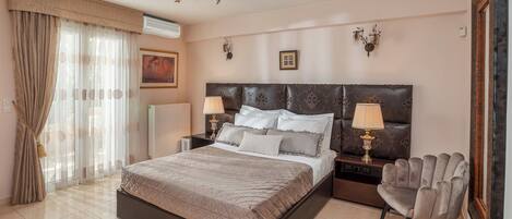 A hotel room with a large bed, two bedside tables with lamps, a chair, a radiator, and a window with curtains.