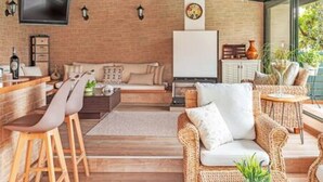 A modern living area with a brick wall, a flat-screen TV, wicker furniture, and a wooden bar. - Villa Stachy & Elia with Heated Pool, by Estia (Malevizi)