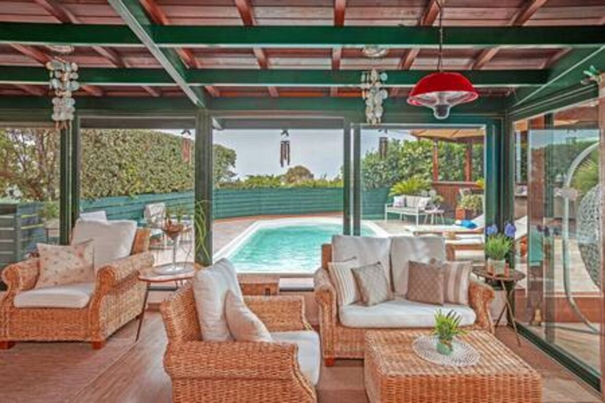 A covered outdoor seating area with wicker furniture, a pool, and a view of the outdoors.