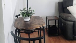 A room with a wooden dining table, a potted plant, a lamp, a chair, a sofa, and a small table.