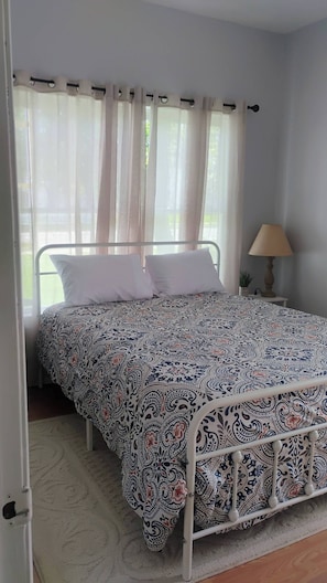 A bed with a patterned bedspread, a bedside lamp, and sheer curtains.
