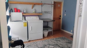 A laundry area with a washing machine, a dryer, a shelf with cleaning supplies, and a door to another room.