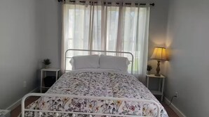 A single bed with a floral bedspread, a bedside lamp, and a small plant on a bedside table.