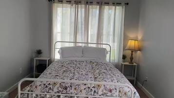Un lit simple avec une couvre-lit à motifs floraux, une lampe de chevet et une petite plante posée sur une table de chevet.