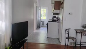 A hallway leading to a kitchen with a refrigerator, a coffee machine, and a dining area with chairs.