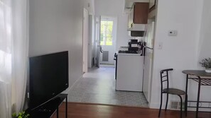A hallway leading to a kitchen with a refrigerator, a coffee machine, and a dining area with chairs.