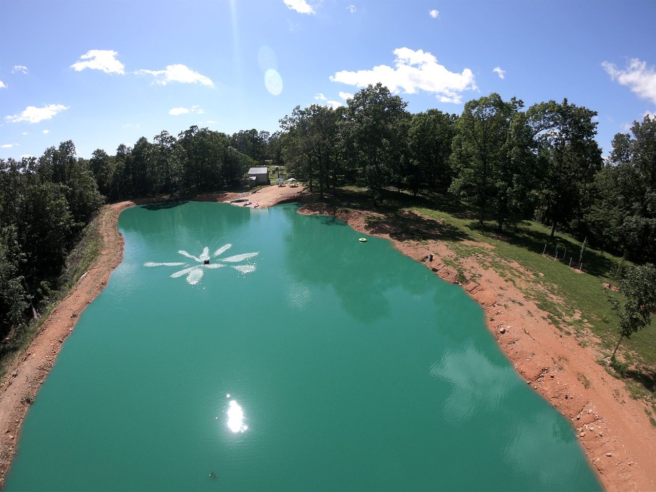 Un extenso cuerpo de agua con un patrón blanco marcado, rodeado de árboles y un pequeño edificio a lo lejos.