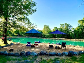 A sandy beach area with two blue umbrellas, a pool, and several chairs. - Tranquil Lakefront Cabin Surrounded by Woods, Wildlife & Scenic Trails in  Williford, Arkansas (Williford)
