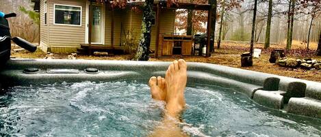 Un jacuzzi con terraza de madera y una casa al fondo.