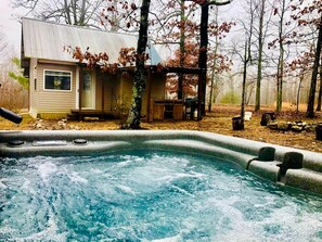 A hot tub with a wooden deck, a small building with a porch, and trees in the background. - Tranquil Lakefront Cabin Surrounded by Woods, Wildlife & Scenic Trails in  Williford, Arkansas (Williford)